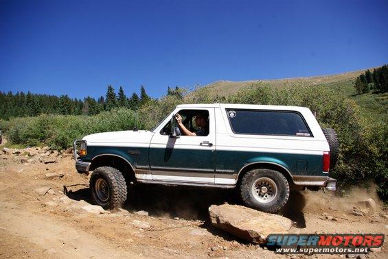 White and green 1996 Ford Bronco side view, off-roading on a rocky trail
