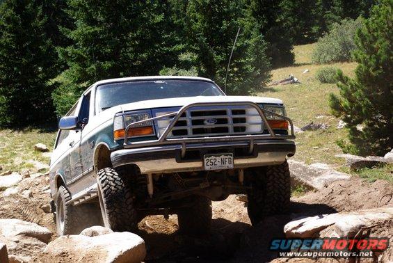 White and teal Ford Bronco with a brush guard navigating rocky terrain