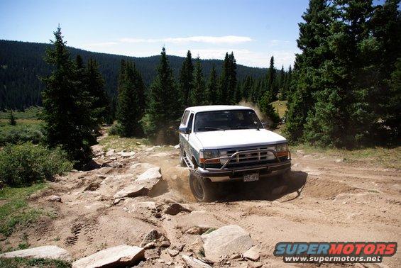 White Ford Bronco driving on a rocky mountain trail, kicking up dust