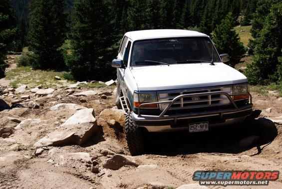 White Ford Bronco with a brush guard navigating a rocky, off-road trail
