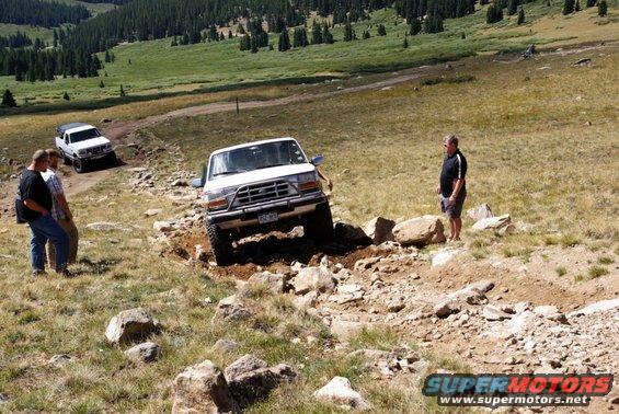White Ford Bronco navigating rocky terrain, front grille visible