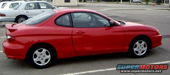 Red coupe with a rear spoiler parked in a lot. A silver sedan is behind it