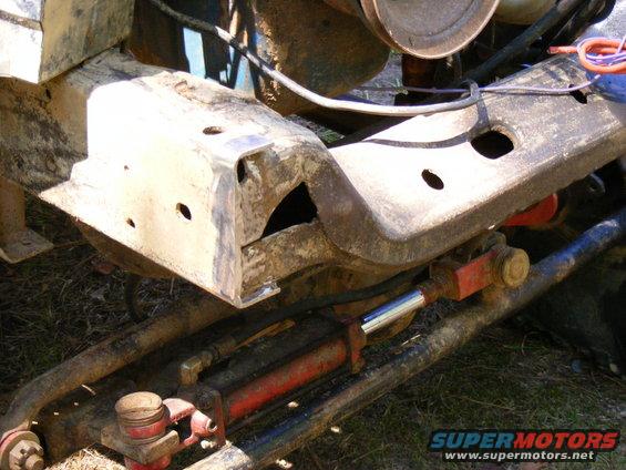 Close-up of a vehicle's rusty frame with steering parts, including a red hydraulic cylinder