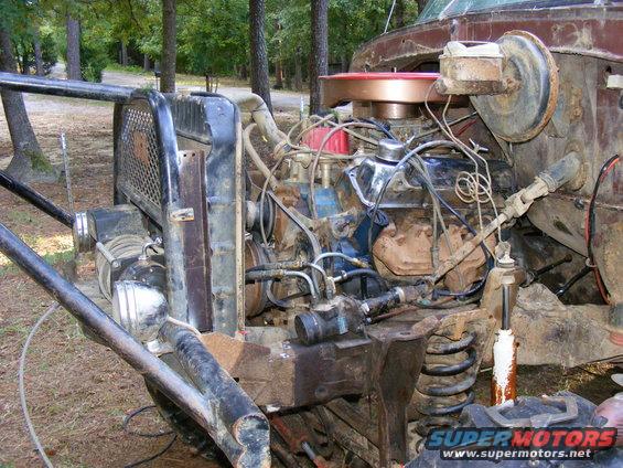 Engine bay of a rusty vehicle with a large V8 engine, exposed radiator, and custom roll cage