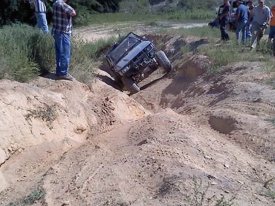Silver off-road SUV with roll cage descending a steep dirt embankment, tires angled
