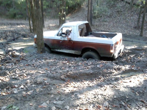 1989 Ford Bronco stuck in muddy terrain with trees around