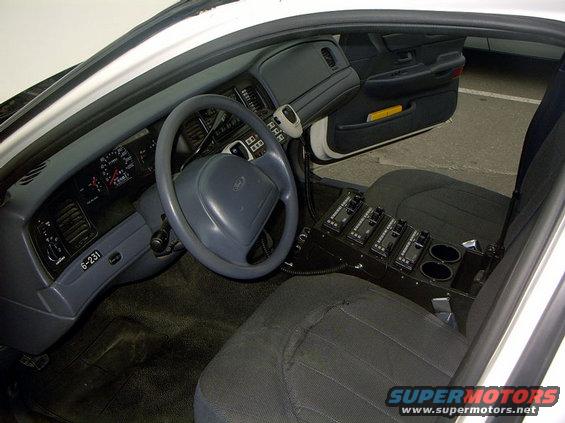 Interior of a 1999 Ford Crown Victoria police car, showing dashboard, steering wheel, and center console with radio equipment