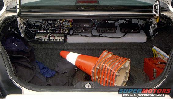 Trunk interior with wiring, radio equipment, traffic cones, and a spare tire