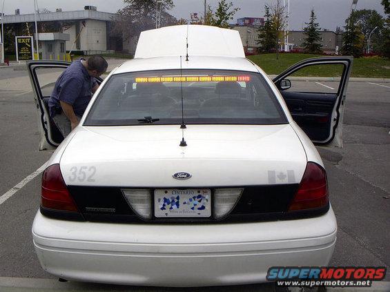 Rear of a white 1999 Ford Crown Victoria police car with doors open and hood up. Ontario license plate visible