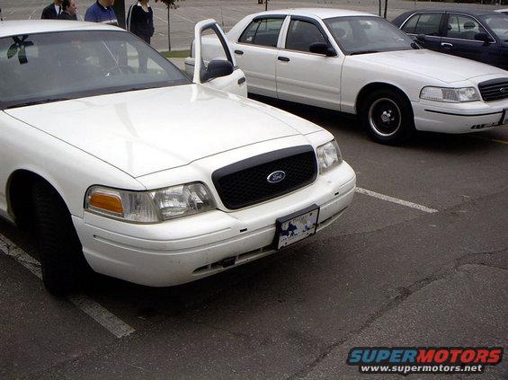 White Ford Crown Victoria with black grille, parked in a lot. Front view