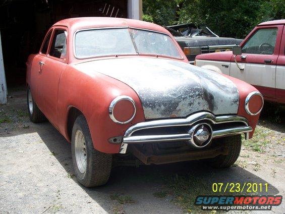 Red coupe with a weathered hood and chrome grille, parked outdoors