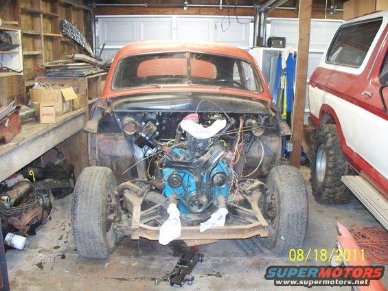 Old car with engine exposed in a garage, next to a red and white Ford Bronco