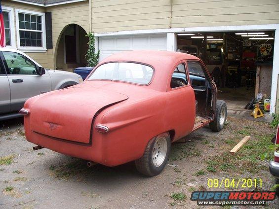 Red coupe with fins and a split rear window, missing doors and hood, parked in a driveway