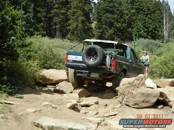 Dark green Ford Bronco with a spare tire on the back, navigating a rocky trail