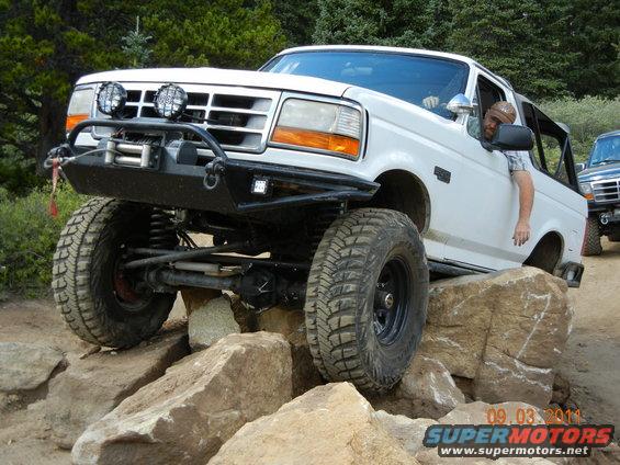 1996 Ford Bronco with aftermarket bumper and winch navigating large rocks, another vehicle visible behind