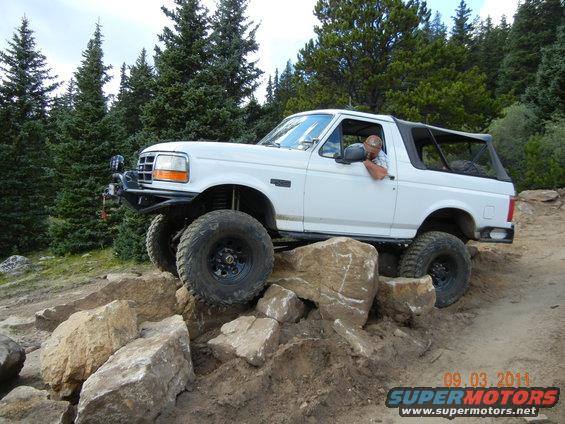 White 1996 Ford Bronco on rocks, driver visible