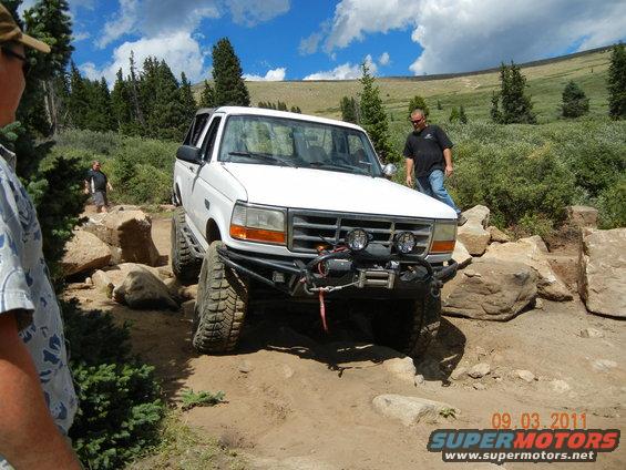 White 1996 Ford Bronco navigating a rocky trail with a man standing nearby