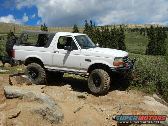 White 1996 Ford Bronco with soft top on a rocky trail, front bumper modified