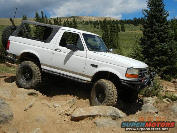 White 1996 Ford Bronco navigating a rocky trail with a spare tire on the back