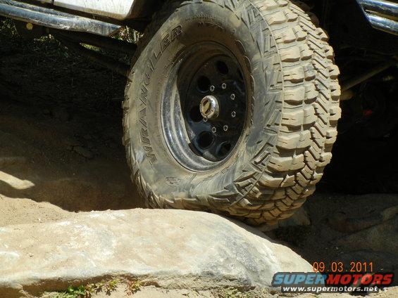 Close-up of a knobby off-road tire on a black rim, angled over a rock