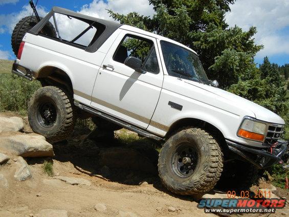 1996 Ford Bronco climbing over rocks on a trail, with a spare tire mounted on the back