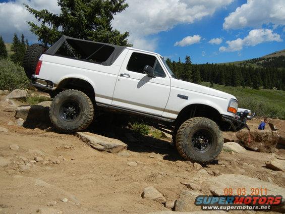 White Ford Bronco with a soft top, lifted suspension, and large tires, climbing a rocky incline