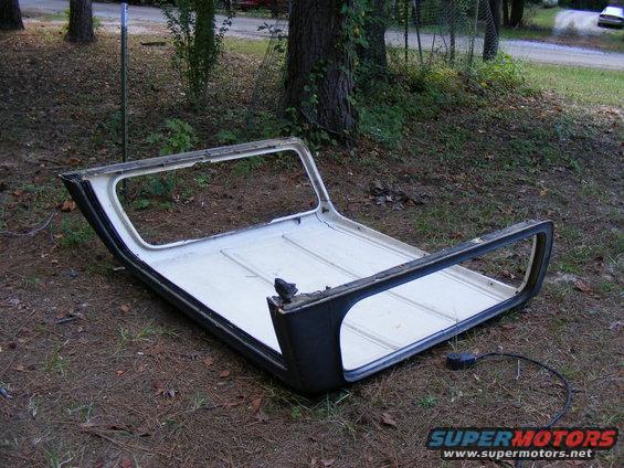Vehicle hardtop lying on the ground outdoors. It is white on the inside and black on the outside with large window openings