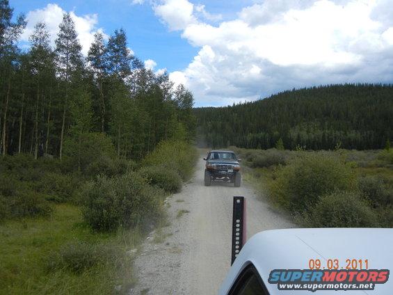 Dark green Ford Bronco driving on a dirt road, lifted suspension, off-road tires