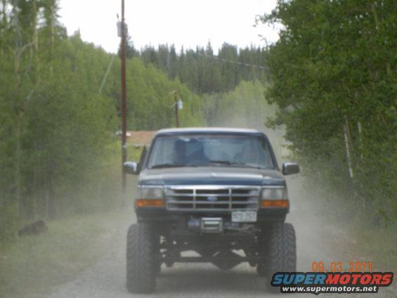 Lifted Ford pickup truck driving on a dirt road, kicking up dust