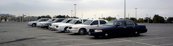 Dark blue 1998 Ford Crown Victoria parked in a lot with other white Crown Victorias