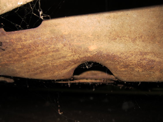 Close-up of heavily rusted metal frame with cobwebs, showing a curved cutout