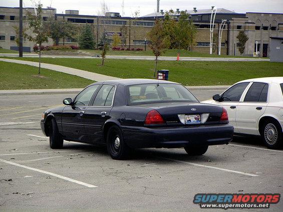 Dark blue Ford Crown Victoria, rear view, parked next to a white car. The Crown Victoria appears to be a 2000 model year