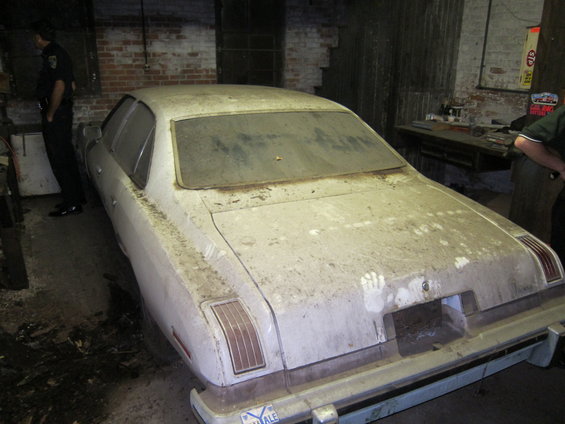 Dust-covered white sedan, rear view. Handprints visible on trunk