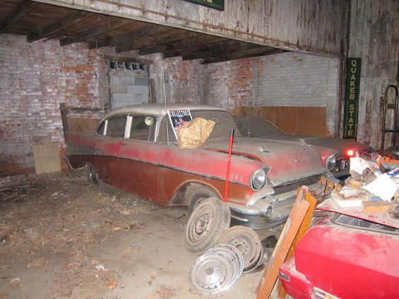 Dusty red and white 1957 Chevrolet Bel Air parked inside a garage with other cars and parts