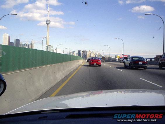 Red sedan driving on a highway with Toronto skyline in background