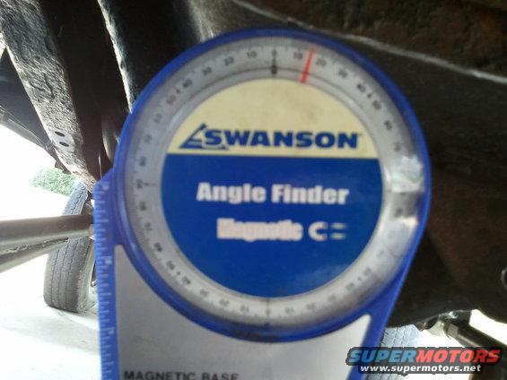 Blue angle finder tool attached to rusty vehicle frame near tire