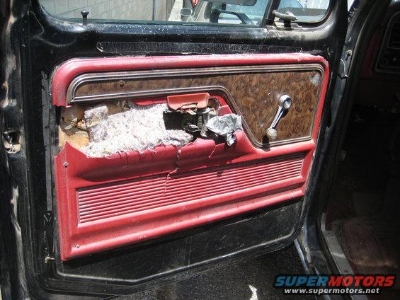 Interior door panel with torn upholstery and exposed insulation. Chrome window crank visible