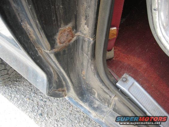 Door jamb of a vehicle showing rust damage and worn metal trim