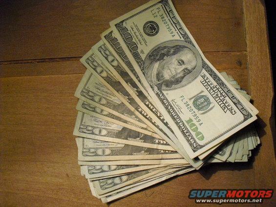 Fan of US dollar bills, including hundreds and twenties, on a wooden surface