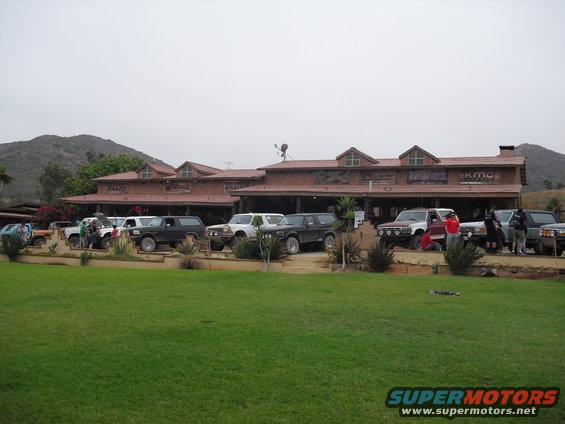 Several SUVs parked in front of a wooden building with mountains in the background. Supermotors.net logo visible