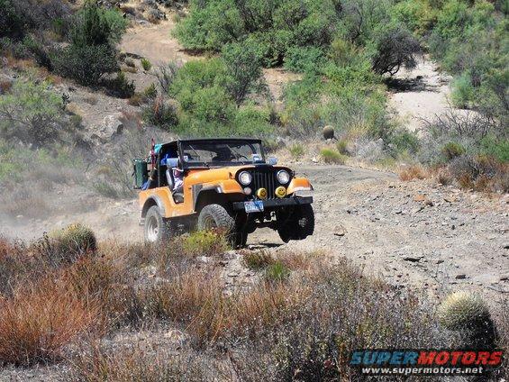 Orange Jeep CJ-7 off-roading on a dusty trail