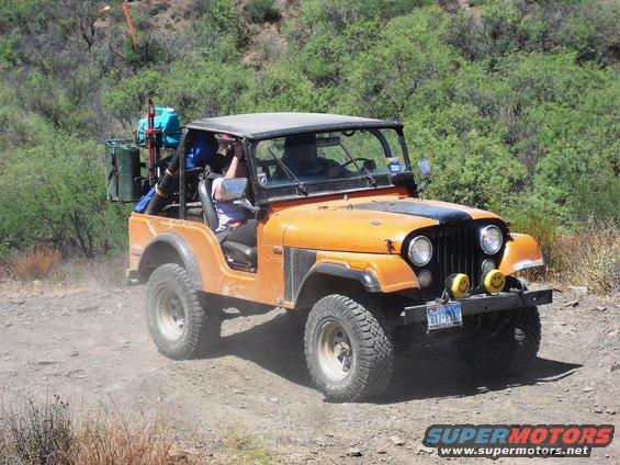 Orange Jeep CJ driving on a dirt road with gear on the back