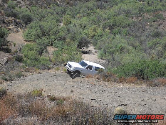 White 1987 Ford Bronco driving off-road on a dirt path
