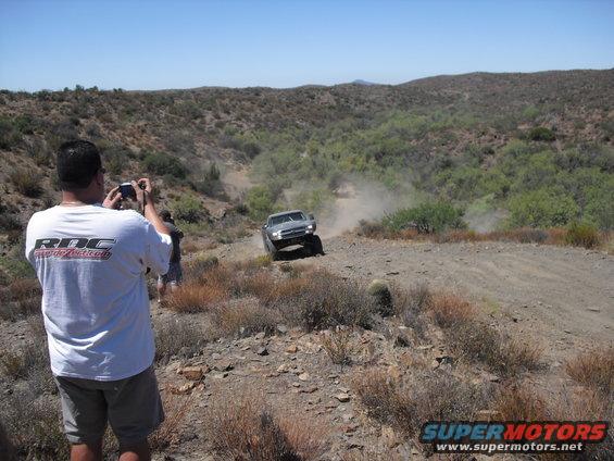 Silver SUV kicking up dust on a desert trail, viewed from a low angle