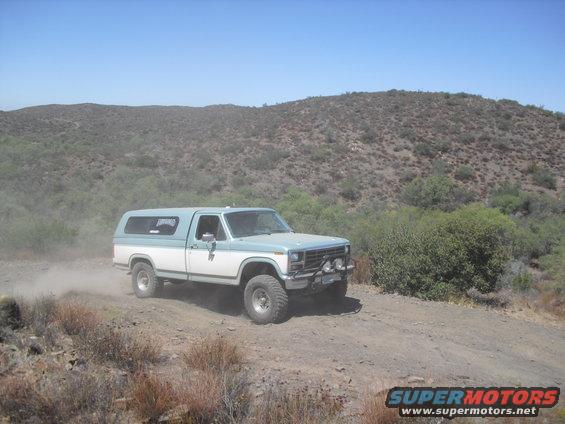 Light blue and white pickup truck with camper shell, lifted suspension, driving off-road