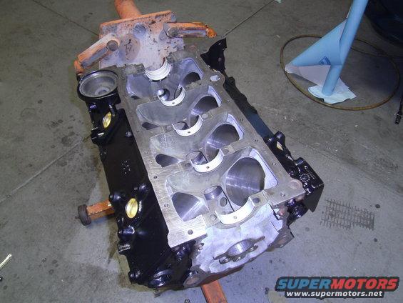 Engine block on an orange stand, showing cylinder bores and bearing caps