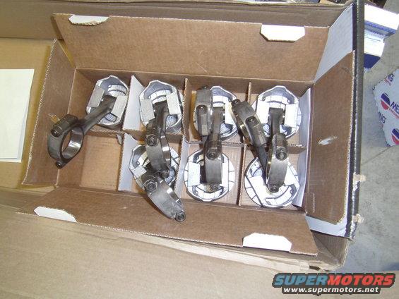 Box of six pistons with connecting rods, some with white paper packaging