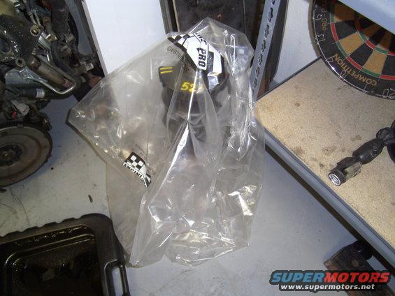 Engine part in a clear plastic bag with 'PRO' and '53' visible, next to a disassembled engine