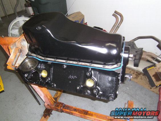 Black engine block with oil pan mounted on an orange engine stand, with exhaust manifolds in the background