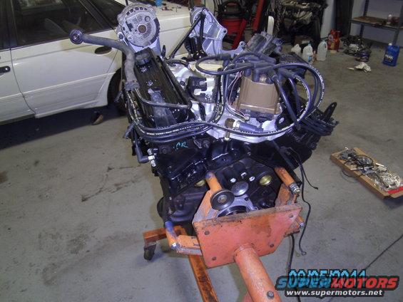 Engine on an orange stand, with a white vehicle partially visible behind it